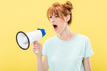 Naklejka premium angry redhead young woman holding megaphone and screaming isolated on yellow