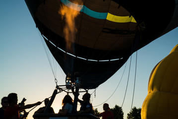 Dark silhouette of sportsman in balloon basket. International meeting of hot air balloons and flying competition. Colourful balloons in the evening skyline. Adventure and freedom, summertime. 