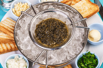 Mediterranean caviar appetizer on ice, toast, butter, greens and a set of sauces