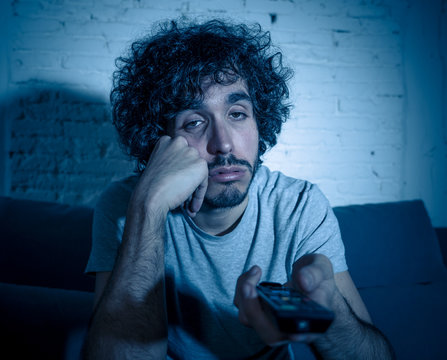 Lifestyle portrait of young millennial man watching boring tv feeling sleepy at night