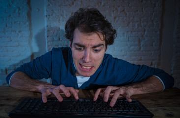 Young man hooked on the computer laptop late at night feeling stressed and sleepless