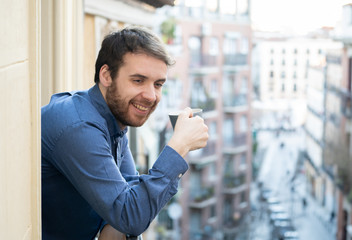 Attractive happy casual young man relaxing at home enjoying the urban view on home balcony