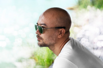 profile of 40s casual adult bald beard wearing sunglasses in white T-shirt with light bokeh of water natural background