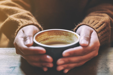 Closeup image of a woman holding a cup of hot coffee on wooden table