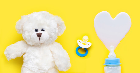 Bottle of milk for baby and baby pacifier with toy bear on yellow background.