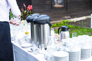 Lot of white porcelain coffee cups and large big thermos on the table in outdoors summer party