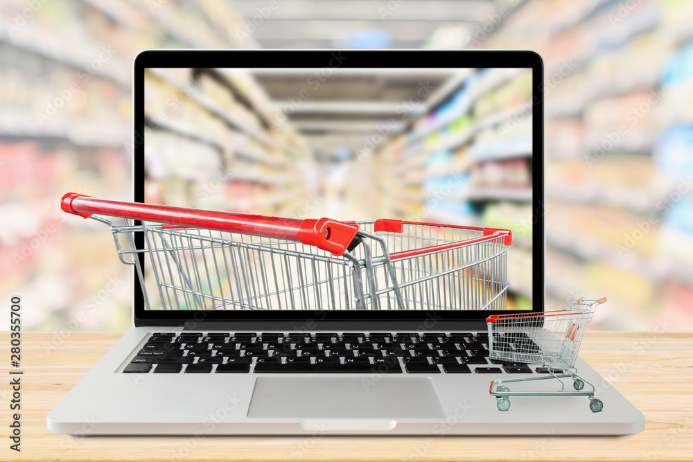 Wall mural supermarket aisle blurred background with laptop computer and shopping cart on wood table grocery on