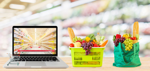 supermarket aisle blurred background with laptop computer and shopping cart on wood table grocery...