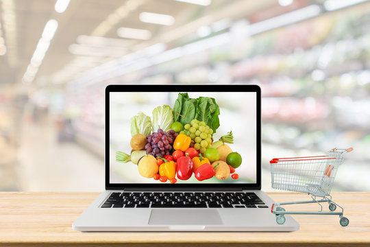 supermarket aisle blurred background with laptop computer and shopping cart on wood table grocery online concept