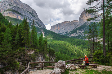 Mother and little daughter sitting on a bench admire a beautiful view of the snow-capped mountains and green spruce in the Dolomites in Italy