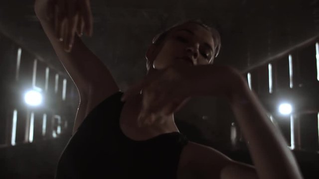 Close-up of ballet dancer as she practices exercises on dark stage or studio. Ballerina shows classic ballet pas. Slow motion. Flare, gimbal shot