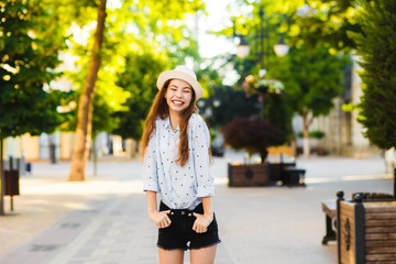 Emotional girl teenager in a hat walks through the summer city. Debonair caucasian girl enjoying...