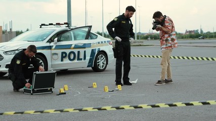 Policemen and forensic analyst collect evidence take pictures and investigate a dreadful crime in the city street outdoors.