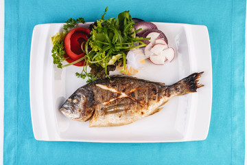 Mediterranean dish, European cuisine. whole fish baked in the oven, served with a salad of vegetables, greens, arugula, onion rings, tomato and lemon