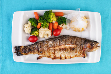 Mediterranean dish, European cuisine. whole fish baked in the oven, served with steamed vegetables - cauliflower, broccoli, carrots, cherry tomatoes and lemon