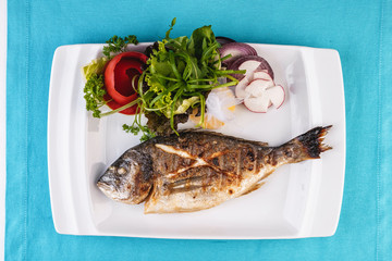Mediterranean dish, European cuisine. whole fish baked in the oven, served with a salad of vegetables, greens, arugula, onion rings, tomato and lemon