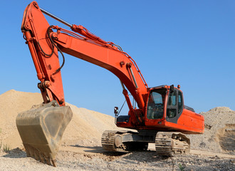 Red excavator between sand dunes and blue sky cloudless  in an open pit mine