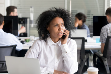 Unhappy African American woman talking on phone at workplace