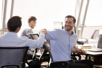 Male colleagues fist bumping at workplace, celebrating teamwork success