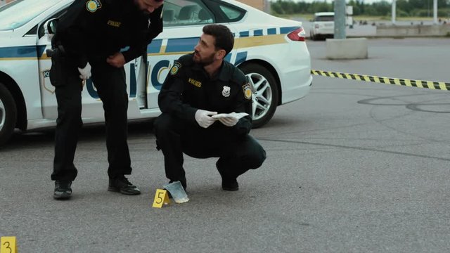 Two police officers colleagues examine illegal drugs as evidence squatting near the police car. Investigation area.