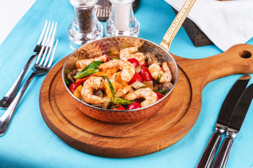 Seafood, Mediterranean cuisine, European dish. Warm salad of grilled fish pieces, shrimps and mussels in a frying pan, with grilled vegetables - with green onions, greens, mushrooms and vegetables.