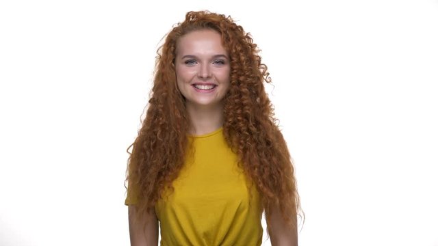 Cheerful young redhair curly lady agreeing with something and shaking her head looking at the camera over white background isolated