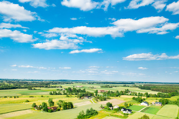 Green fields and trees of Polish countryside stretch to the horizon under white clouds and blue sky