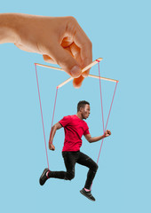 Man like a puppet in somebodies hands on blue background. Concept of unfair manipulation, phycology...