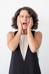 Scared woman looking at camera. Front view of shocked middle aged woman standing with open mouth isolated on grey background. Emotion concept