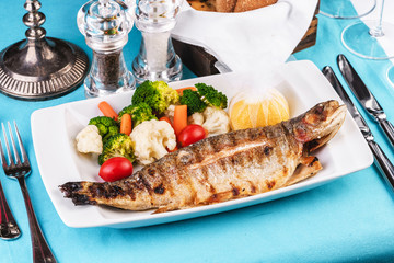 Mediterranean dish, European cuisine. whole fish baked in the oven, served with steamed vegetables - cauliflower, broccoli, carrots, cherry tomatoes and lemon