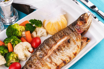 Mediterranean dish, European cuisine. whole fish baked in the oven, served with steamed vegetables - cauliflower, broccoli, carrots, cherry tomatoes and lemon