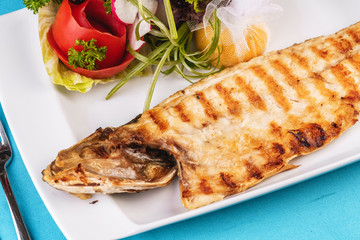 Mediterranean dish, European cuisine. Rainbow trout, grilled, served with vegetables - tomato, lettuce, radish, iceberg cabbage