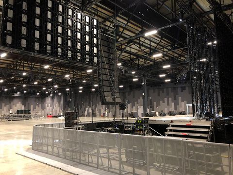 Installation of professional sound speakers, line array and stage equipment for a concert. Backstage area and tech zone with metal barriers.