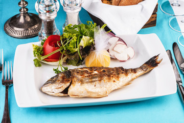 Mediterranean dish, European cuisine. whole fish baked in the oven, served with a salad of vegetables, greens, arugula, onion rings, tomato and lemon