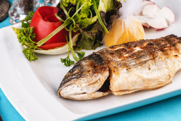 Mediterranean dish, European cuisine. whole fish baked in the oven, served with a salad of vegetables, greens, arugula, onion rings, tomato and lemon