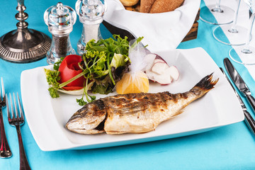 Mediterranean dish, European cuisine. whole fish baked in the oven, served with a salad of vegetables, greens, arugula, onion rings, tomato and lemon