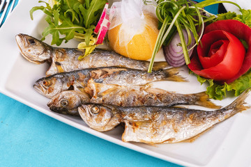 Mediterranean dish, European cuisine. Whole fish grilled capelin, served with a salad of vegetables — greens, arugula, onion rings, tomato, green and yellow pepper and lemon