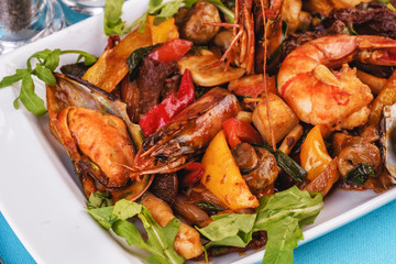 Mediterranean dish, European cuisine. Braised shrimps, mussels, squids with vegetables, red and green pepper, tomatoes, greens, arugula and mushrooms