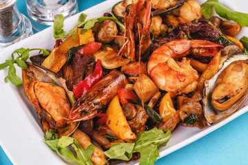 Mediterranean dish, European cuisine. Braised shrimps, mussels, squids with vegetables, red and green pepper, tomatoes, greens, arugula and mushrooms