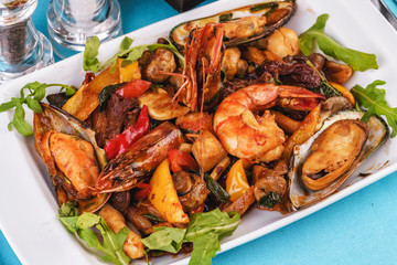 Mediterranean dish, European cuisine. Braised shrimps, mussels, squids with vegetables, red and green pepper, tomatoes, greens, arugula and mushrooms