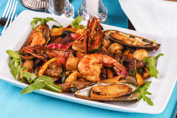 Mediterranean dish, European cuisine. Braised shrimps, mussels, squids with vegetables, red and green pepper, tomatoes, greens, arugula and mushrooms