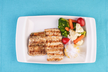 Mediterranean dish, European cuisine. Grilled pieces of fish, served with cooked vegetables - broccoli, cauliflower, cherry tomatoes and lemon