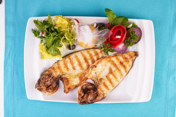European cuisine, Mediterranean dish. River trout steak, white meat fish, served with vegetables, lemon and arugula and tomato salad