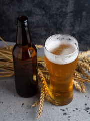 Glass of beer on a dark stone background with beer bottle and wheat