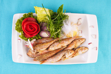 European cuisine, Mediterranean dish. Fried fish in deep fat, capelin in batter with greens, tomatoes, cheese and red onion