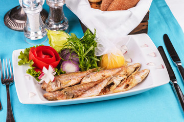 European cuisine, Mediterranean dish. Fried fish in deep fat, capelin in batter with greens, tomatoes, cheese and red onion