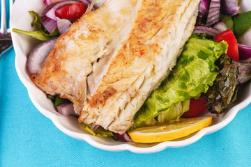 Mediterranean dish, European cuisine. grilled white fish steak on a pillow of lettuce- lemon, arugula, red onion rings, lettuce leaves, cabbage, tomatoes with olive oil