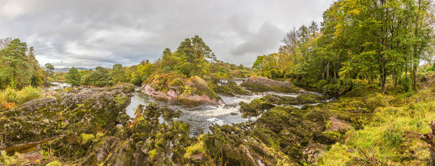 Panorama picture of typical Irish landscape with green vegetation and romantic small water stream