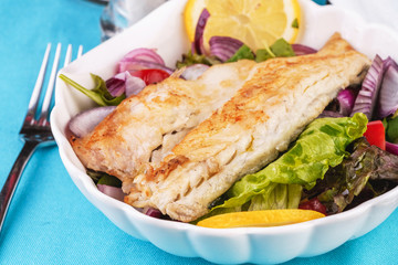 Mediterranean dish, European cuisine. grilled white fish steak on a pillow of lettuce- lemon, arugula, red onion rings, lettuce leaves, cabbage, tomatoes with olive oil