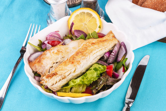 Mediterranean dish, European cuisine. grilled white fish steak on a pillow of lettuce- lemon, arugula, red onion rings, lettuce leaves, cabbage, tomatoes with olive oil